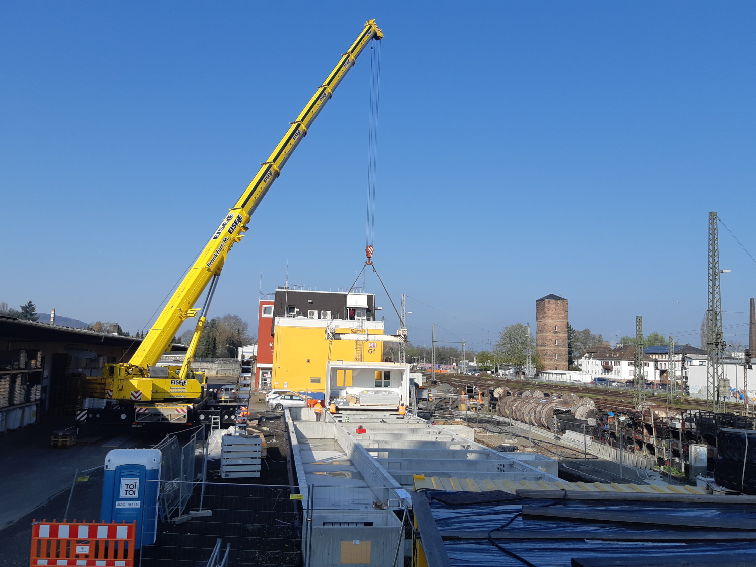 Teaserbild verlinkt auf Seite Baustellen-Journal; ein Mobilkran hebt Betonteile auf einer Baustelle ein